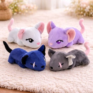 Puede incluir: Cuatro juguetes de peluche con forma de ratón en azul claro, morado, azul oscuro y gris. Cada peluche tiene orejas grandes, una cola larga y ojos bordados. El ratón azul claro tiene una nariz rosa, el morado tiene ojos morados y el azul oscuro tiene ojos amarillos.