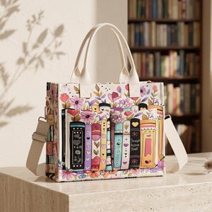 May include: A rectangular tote bag featuring a colourful print of stacked books and floral patterns. The bag has two cream-coloured top handles and an adjustable shoulder strap. One book spine is clearly labelled with the text Straight have Shelf.