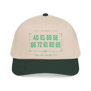 May include: A beige baseball cap with a dark green brim and a dark green button on top. The front features green text that reads HEX ENCODED, followed by the hexadecimal sequence 4D 61 69 6E 66 72 61 6D 65, and the question CAN YOU DECODE IT?