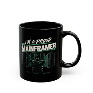Peut inclure: Un mug en céramique noire orné d'un graphique représentant une personne assise face à des baies de serveurs. Le texte indique I'M A PROUD MAINFRAMER avec les mots LEGACY, STABILITY et REAL IMPACT imprimés en petites lettres vertes en bas.