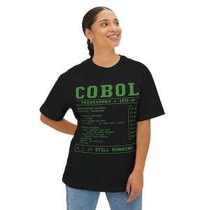 May include: A black short-sleeved t-shirt featuring green text that reads COBOL PROGRAMMER 1970-∞, followed by lines of code including IDENTIFICATION DIVISION, PROGRAM-ID, and the phrase STILL RUNNING at the bottom in a retro computer terminal font.