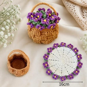 May include: A crocheted tan basket filled with purple flowers, a small empty tan basket, and a round white crocheted coaster with a purple floral border. A black line with the text 16cm indicates the coaster width is 16 centimetres.