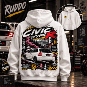 Puede incluir: Una sudadera con capucha blanca que presenta un gráfico en la espalda de un coche hatchback blanco, una montaña, flores de cerezo y texto que incluye "CIVIC TYPE R", "GOOD CARS BETTER DAYS" y "SAME SPIRIT". El frente tiene un pequeño logo "R" amarillo.