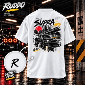 May include: A white t-shirt featuring a graphic print of a black Toyota Supra MK4 car on a city street with a red sun, Japanese text, and the words Toyota Supra MK4, Legends Never Fade, and Power Culture People Forever. A circular inset shows a black letter R.