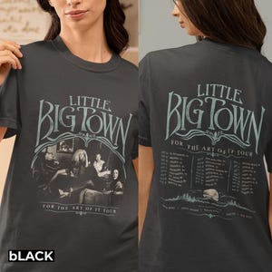 以下が含まれることがあります： Little Big Town For The Art Of It Tourの文字が入ったチャコールグレーのTシャツ。前面にはバンドの白黒写真がプリントされています。背面には、水色の文字でツアーの日程と場所が記載されており、月のグラフィックが描かれています。