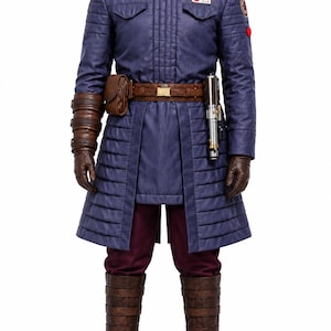 Può includere: Un lungo cappotto blu scuro con colletto in pelliccia sintetica, indossato sopra pantaloni bordeaux e stivali in pelle marrone. L'outfit include una cintura marrone con tasca, guanti in pelle marrone con protezioni e un'elsa di spada laser.