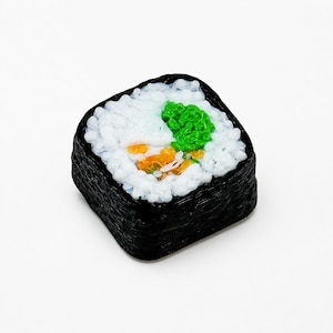 May include: A square-shaped sushi roll replica featuring a dark black outer layer of seaweed, a thick filling of white rice, a bright green textured center, and small orange accents nestled within the white rice grains.
