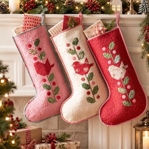May include: Three quilted Christmas stockings hanging in a row. The left stocking is red and white gingham, the center is cream with a swirling pattern, and the right is solid red. Each features a fabric bird and green leaf applique.