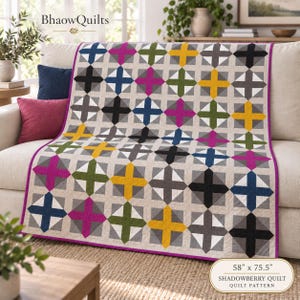 May include: A quilt featuring a repeating pattern of multicoloured crosses in yellow, magenta, olive green, navy blue, and charcoal grey on a light beige background, finished with a bright purple border and measuring 147 cm by 192 cm.