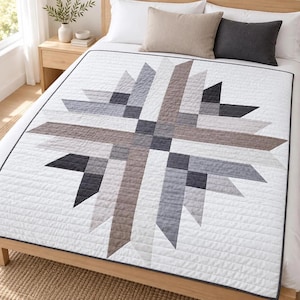 May include: A white quilt featuring a large, geometric star pattern composed of various shades of gray, charcoal, and taupe fabric strips. The quilt has a thin dark gray border and horizontal channel stitching throughout the entire surface.