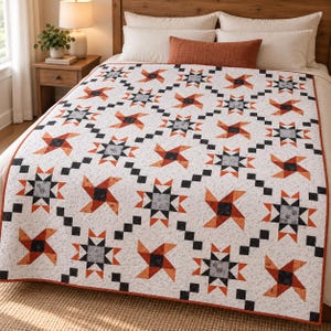 Könnte beinhalten: Eine Steppdecke mit einem wiederkehrenden Muster aus orangefarbenen und anthrazitgrauen Stern- und Windradblöcken auf weißem Grund mit gesprenkelter Textur. Das Design umfasst diagonale Reihen kleiner schwarzer Quadrate und eine orangefarbene Umrandung.