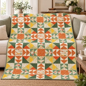 Op de afbeelding: Een rechthoekige quilt met een geometrisch patchworkpatroon van driehoeken en vierkanten. Het ontwerp bevat een kleurenpalet van oranje, donkergroen, geel en crème, met bloemmotieven en kleine prints gerangschikt in een herhalend raster.