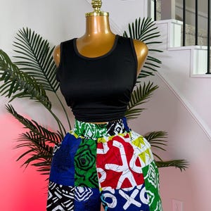 May include: A black sleeveless tank top paired with high-waisted shorts featuring a vibrant patchwork pattern. The shorts display a mix of red, blue, green, white, and black geometric and abstract motifs with a distinct batik-style aesthetic.
