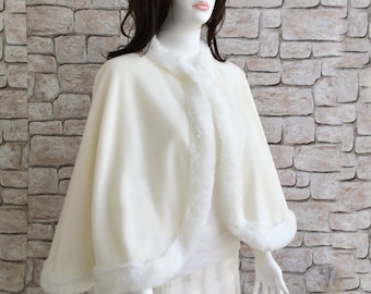 May include: A white faux fur bridal cape with a white fleece lining. The cape has a rounded collar and a scalloped hem.