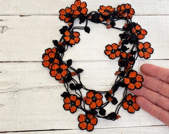 May include: A black crocheted necklace with orange flower accents and brown beads.
