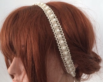 May include: A white headband with a delicate lace design and pearl accents. The headband is worn on a mannequin with red hair.
