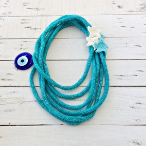 May include: A turquoise blue knitted rope necklace with a white and blue crocheted star charm and a blue evil eye charm.