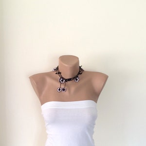 May include: A black choker necklace with white flower accents. The necklace is on a white mannequin.