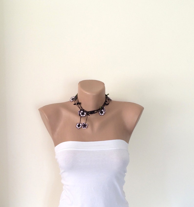 May include: A black choker necklace with white flower accents. The necklace is on a white mannequin.