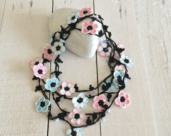 May include: A multi-strand necklace made of black string with crocheted flowers in pink, blue, and white.