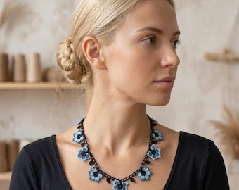May include: A handmade crochet necklace featuring a series of light blue flowers with dark blue centres, connected by a delicate black thread chain. The floral pattern is repeated along the entire length of the necklace, creating a continuous design.