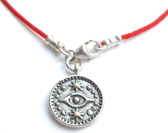 May include: A red string bracelet with a silver charm featuring an eye with stars around it.