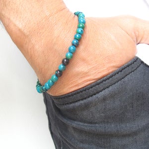 Puede incluir: Un brazalete con cuentas azules y negras. El brazalete se lleva en la muñeca.