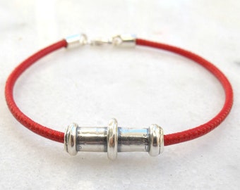 May include: A red leather bracelet with a silver cylindrical charm. The charm has three rings around it.