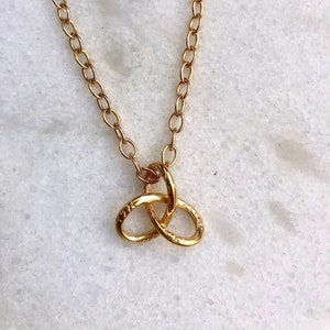 May include: A gold chain necklace with a gold knot pendant. The knot is a simple design with two loops that are intertwined.