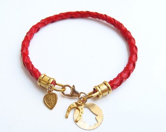 May include: A red braided leather bracelet with gold-toned charms, including a heart, horseshoe, and bell.