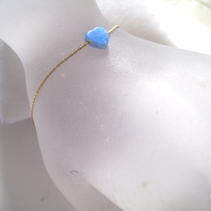 May include: A delicate gold chain necklace with a light blue heart-shaped opal pendant.