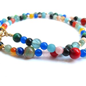 Pode incluir: Um colar de contas multicoloridas com um fecho dourado e um pequeno amuleto dourado. As contas s&atilde;o feitas de v&aacute;rias pedras preciosas, incluindo azul, verde, vermelho, laranja e preto.