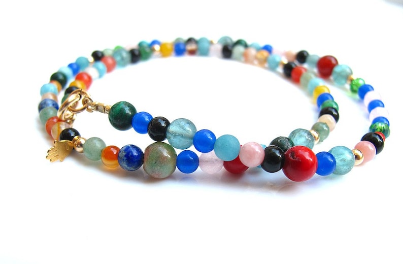 Pode incluir: Um colar de contas multicoloridas com um fecho dourado e um pequeno amuleto dourado. As contas s&atilde;o feitas de v&aacute;rias pedras preciosas, incluindo azul, verde, vermelho, laranja e preto.