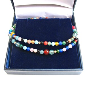 Pode incluir: Um colar de contas multicolorido com uma variedade de pedras, incluindo verde, azul, vermelho e amarelo, em uma caixa de joias de veludo azul.