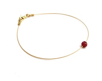 Op de afbeelding: Een delicate gouden ketting met een enkele rode edelsteen kraal.