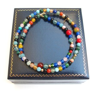 Pode incluir: Um colar de contas multicolorido com uma variedade de pedras, incluindo turquesa, vermelho, verde e azul, em uma caixa de joias de veludo azul.