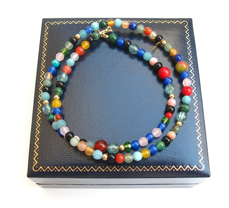 Pode incluir: Um colar de contas multicolorido com uma variedade de pedras, incluindo turquesa, vermelho, verde e azul, em uma caixa de joias de veludo azul.