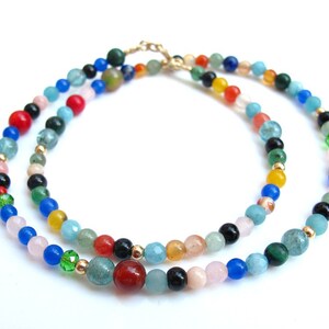 Pode incluir: Um colar de v&aacute;rias voltas feito de contas de pedras preciosas coloridas. O colar apresenta uma variedade de cores, incluindo azul, verde, vermelho, laranja, amarelo e rosa. As contas s&atilde;o de diferentes formas e tamanhos, e s&atilde;o enfiadas em uma corrente de ouro.