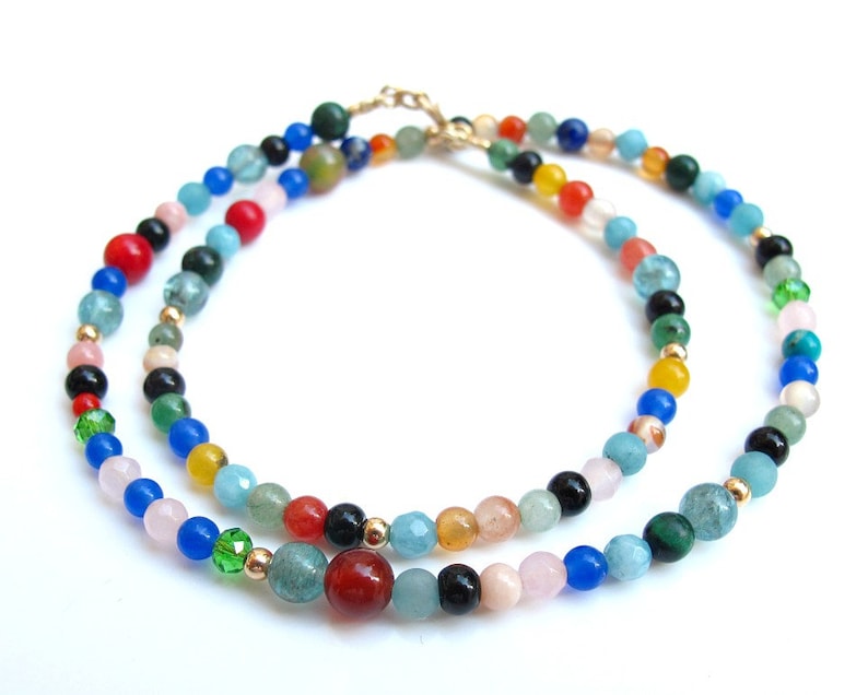 Pode incluir: Um colar de v&aacute;rias voltas feito de contas de pedras preciosas coloridas. O colar apresenta uma variedade de cores, incluindo azul, verde, vermelho, laranja, amarelo e rosa. As contas s&atilde;o de diferentes formas e tamanhos, e s&atilde;o enfiadas em uma corrente de ouro.