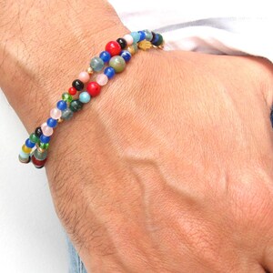 Pode incluir: Um bracelete de contas multicoloridas com um fecho dourado. O bracelete &eacute; feito com v&aacute;rias pedras, incluindo vermelho, azul, verde e rosa.