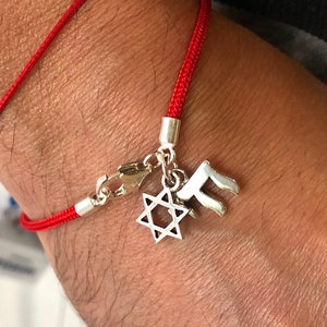 May include: A red string bracelet with a silver charm featuring a Star of David and the Hebrew letter 'Chai'.