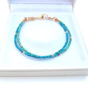 Peut inclure: Un bracelet à double rang de perles turquoise avec des accents dorés. Le bracelet est dans une boîte blanche.