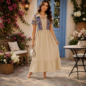 Puede incluir: Un vestido largo de color beige con mangas cortas, cuello camisero y cierre frontal de botones. El cuerpo presenta un estampado geométrico en azul y blanco en los hombros y el pecho, mientras que la falda tiene un bajo con volantes.