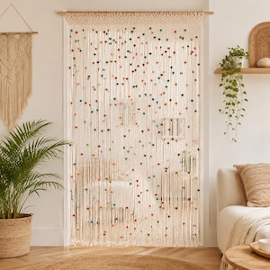 May include: A macrame door curtain made of off-white cotton cord, featuring a woven top section and long, vertical hanging strands. The curtain is decorated with numerous small, colourful beads in shades of red, blue, green, and yellow.