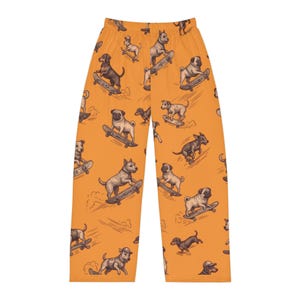 Op de afbeelding: Oranje loungebroek met een herhalend patroon van verschillende hondenrassen, waaronder mopshonden en teckels, op skateboards. De illustraties zijn uitgevoerd in een donkerbruine schetsstijl op een effen oranje achtergrond.