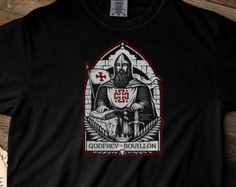 May include: A black short-sleeve t-shirt featuring a graphic print of a medieval knight in armor with a beard, holding a sword and a book. The design includes a red cross emblem, a flag, and the text "GODFREY of BOUILLON" in a gothic arch frame.