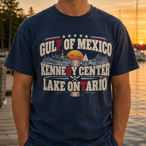 May include: A navy blue short-sleeve t-shirt featuring a graphic print with the text GULF OF MEXICO, KENNEDY CENTER, and LAKE ONTARIO. The design includes a sunset over water, a lighthouse, a sailboat, and crossed oars in a vintage style.