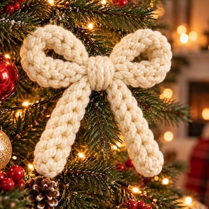 May include: A cream-colored bow ornament crafted from thick, braided rope. The bow features two symmetrical loops at the top and two dangling tails at the bottom, all constructed from a continuous, textured, twisted cord material.