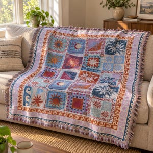 May include: A woven throw blanket featuring a grid of square panels with various sun, moon, and celestial motifs in shades of blue, orange, red, and purple. The blanket has a decorative Greek key border and a fringed edge on all four sides.