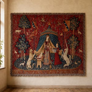 Puede incluir: Un tapiz tejido rectangular con fondo rojo que presenta una tienda azul central, una persona con vestido largo, un león y un unicornio. La escena incluye varios árboles, animales pequeños y motivos florales con bordes de flecos.